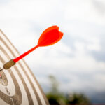 Close up shot red darts arrows in the target of dartboard center on dark blue sky background. Business target or goal success and winner concept.